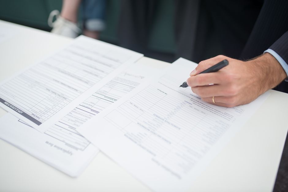 Decisões da Presidência — Close-up of a hand signing insurance documents in an office setting.